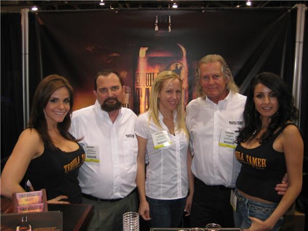 Five people pose in a booth in front of a dark Tequila Tamer backdrop: two men in white shirts, a blonde woman in the center, and two women in black Tequila Tamer tops.