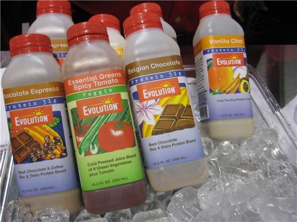Bottles of Evolution drinks with red caps rest in ice, including Chocolate Espresso, Essential Greens Spicy Tomato, Belgian Chocolate and Vanilla Chai flavors.