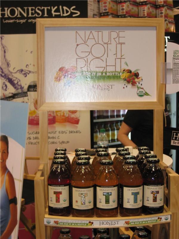 Wooden shelf display with a sign reading "Nature Got It Right" above bottles of Honest Tea in a row, with Honest Kids signage behind and a person in dark clothing in the background.