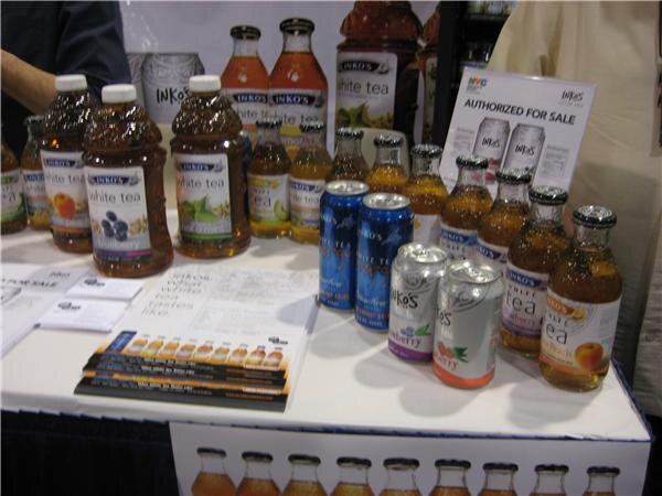 Table display of Inko's white tea in large and small bottles and cans in several flavors, with printed brochures and an "Authorized for sale" sign.
