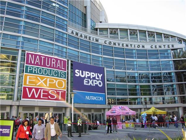 Entrance of the Anaheim Convention Center with large banners for Natural Products Expo West and Nutracon Supply Expo. People walk outside, and a pink tent stands in the background.