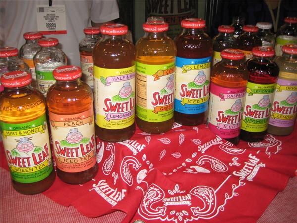 Rows of Sweet Leaf iced tea and lemonade bottles in flavors such as Mint & Honey, Peach, Half & Half and Raspberry stand on a red Sweet Leaf bandana.