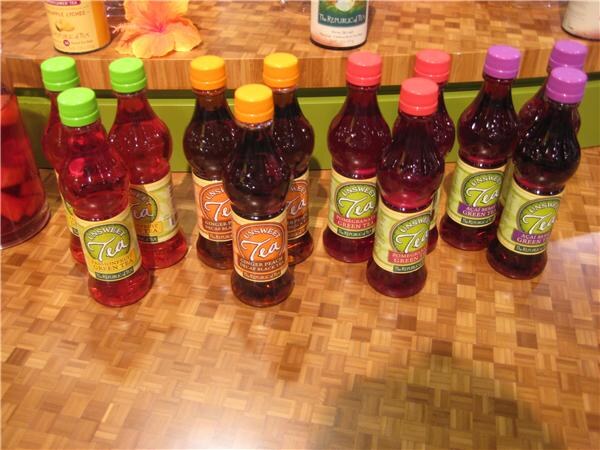 Rows of The Republic of Tea Unsweet Tea bottles with green, orange, red and purple caps stand on a parquet-patterned counter.