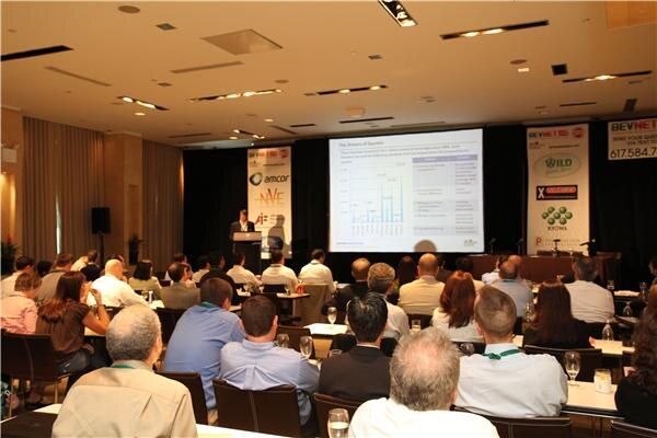 Seated attendees face a speaker at a podium and a projected slide with a bar chart. Sponsor banners show Amcor, NVE Pharmaceuticals, Velcorin and Kyowa.