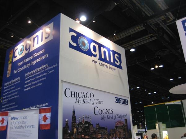 Corner of a large blue and white Cognis booth with the tagline "we know how", a list of ingredients, small Canadian flags and a Chicago skyline graphic reading "Cognis, My Kind of Supplier!".