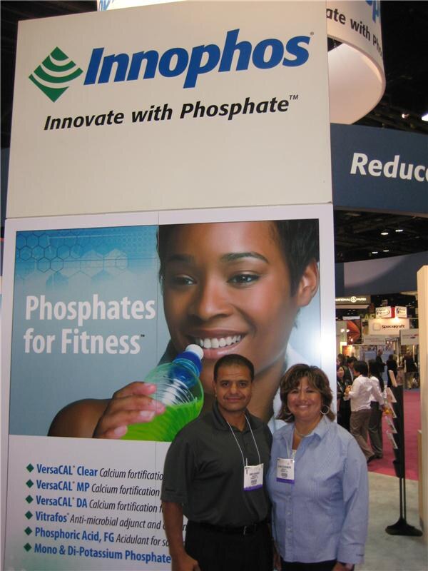 A man and a woman wearing badges stand beneath an Innophos sign reading Innovate with Phosphate, next to a Phosphates for Fitness panel listing VersaCAL and Vitrafos products.