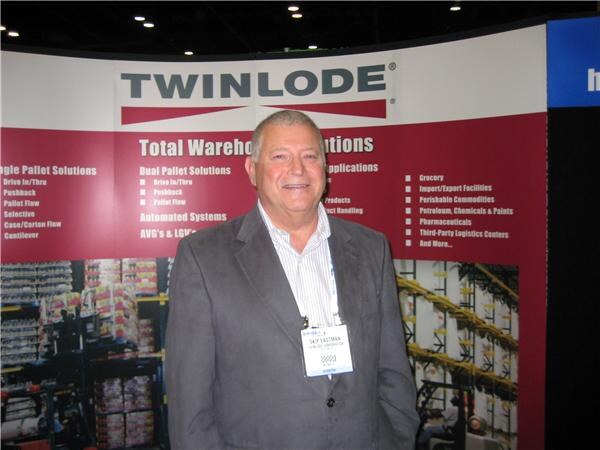 Skip Eastman, in a gray blazer and striped shirt with a badge, stands smiling in front of a Twinlode banner listing warehouse and pallet solutions.