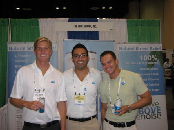 Three smiling men wearing badges stand in front of The Chill Group, Inc. booth banners about natural stress relief. Two of them hold cans.