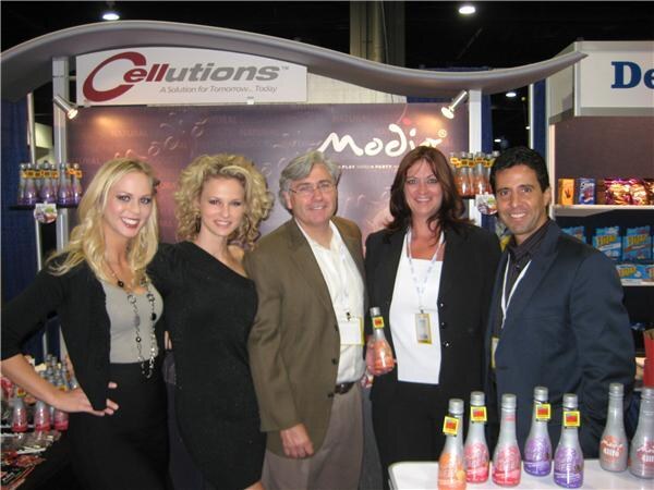 Five people pose in front of the Cellutions booth with a Modjo backdrop, with bottles of Modjo drinks on a table in front of them.