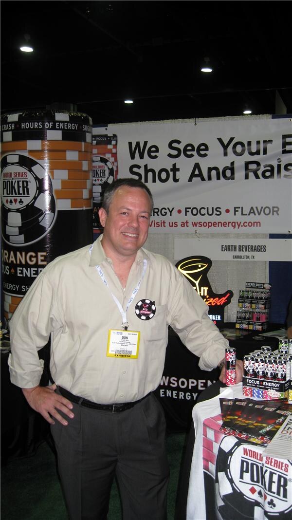 A smiling man named Don, wearing a badge and lanyard, stands beside World Series of Poker WSOP Energy displays and cans in the Earth Beverages booth, with a banner behind him.