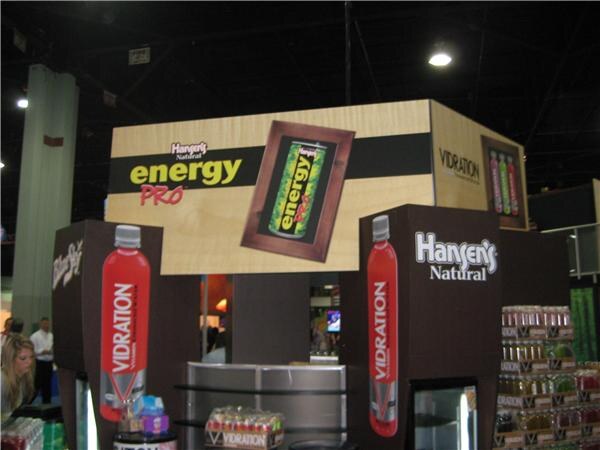 A booth structure with Hansen's Natural, Energy Pro and Vidration signage, large red Vidration bottle graphics, and shelves of product below.