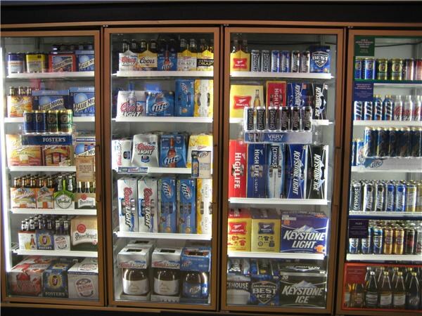 Four glass-door coolers stocked with packs of Coors Light, Miller Lite, Keystone Light, Miller High Life, Foster's, Blue Moon and Keystone Ice beer, plus cans and bottles on the shelves.