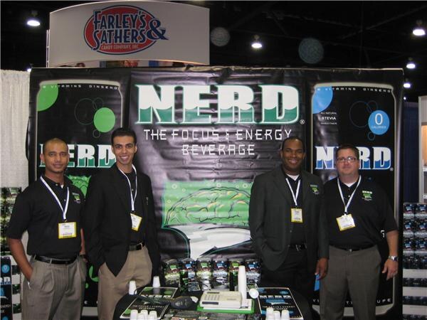 Four men with badges stand at a booth with black Nerd focus and energy beverage banners. A Farley's & Sathers Candy Company sign hangs overhead.