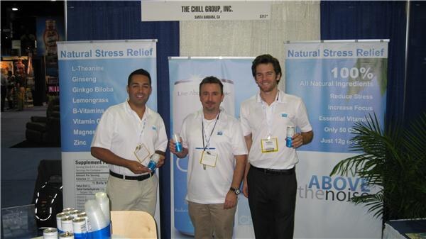 Three men in white polo shirts hold cans in front of Natural Stress Relief banners at The Chill Group, Inc. booth.