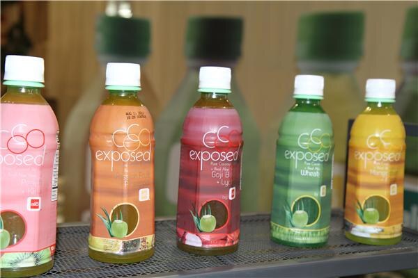 Five plastic bottles of Exposed pure coconut and red aloe drink in pink, orange, red, green and yellow labels stand in a row on a metal mesh shelf.