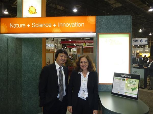 A man in a dark suit and tie and a woman with curly hair and a badge stand under an orange sign reading Nature + Science + Innovation. A DSM sign is visible in the background.