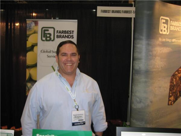 A smiling man in a light blue shirt and exhibitor badge stands in front of Farbest Brands banners with the FB logo.