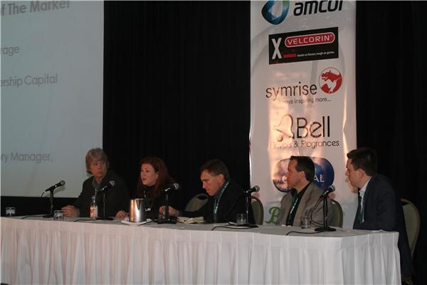 Five people sit at a draped table with microphones during a panel session. A banner behind them shows Velcorin, Symrise and Bell Flavors & Fragrances logos, and a projected slide is at left.