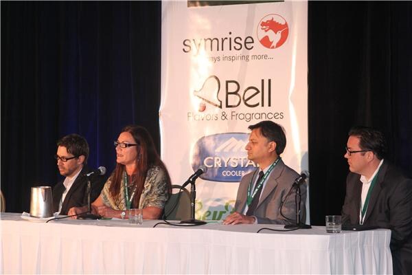 Four panelists sit at a draped table with microphones; a woman in the second seat speaks. Behind them is a banner with Symrise and Bell Flavors & Fragrances logos.
