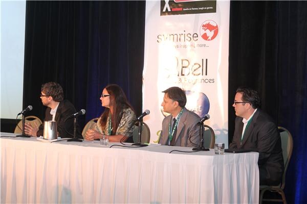 Four panelists seated at a draped table with microphones, photographed from an angle, with a Symrise banner behind them and lanyards around their necks.
