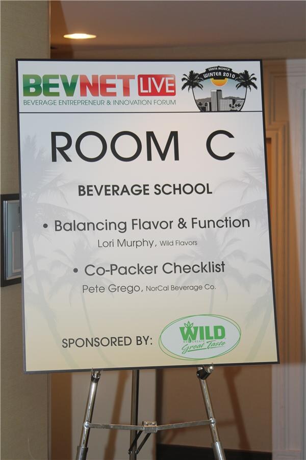 Easel sign reading Room C, Beverage School: Balancing Flavor & Function with Lori Murphy of Wild Flavors, and Co-Packer Checklist with Pete Grego of NorCal Beverage Co., sponsored by Wild.