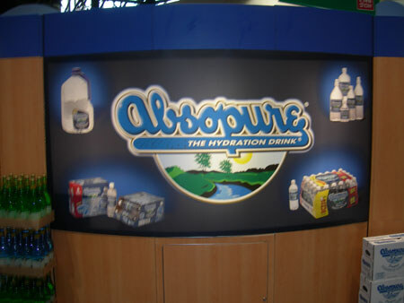 A curved booth wall displays an Absopure The Hydration Drink sign with images of water jugs and bottle packs; cases of Absopure sit at lower right.