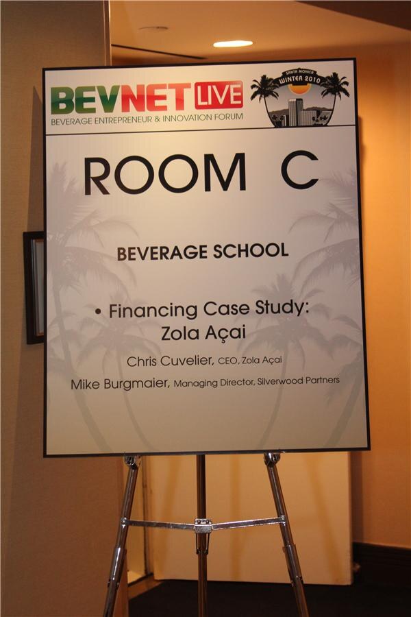 Easel sign reading Room C, Beverage School, Financing Case Study: Zola Açaí, listing Chris Cuvelier, CEO of Zola Açaí, and Mike Burgmaier, Managing Director of Silverwood Partners.