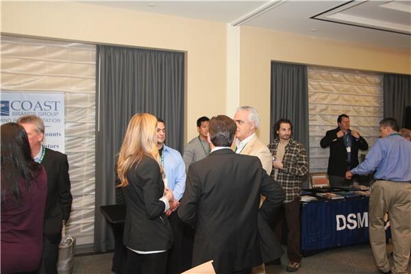 Attendees stand talking in a ballroom, with a Coast Brands Group banner on the left and a blue DSM-draped table on the right.