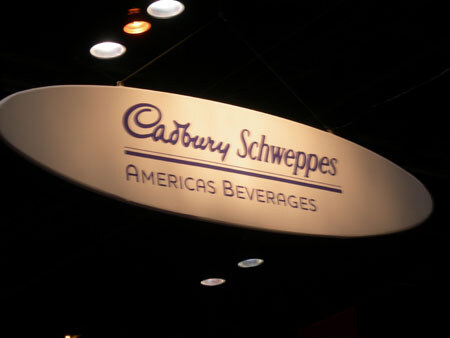 An oval hanging sign reading 'Cadbury Schweppes Americas Beverages' is lit against a dark ceiling with small lights.