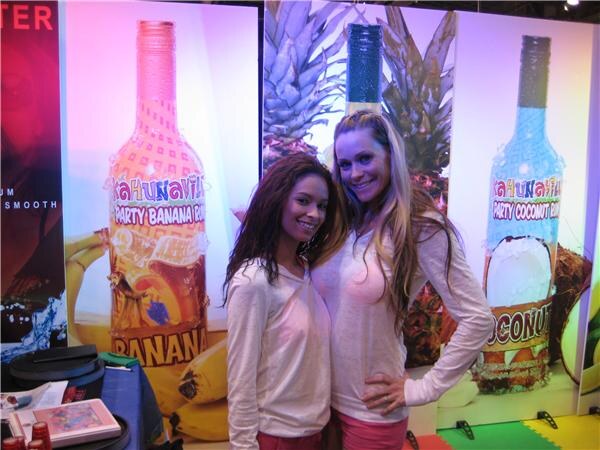 Two smiling women stand in front of large lit Kahunaville Party Banana Rum and Party Coconut Rum bottle displays.