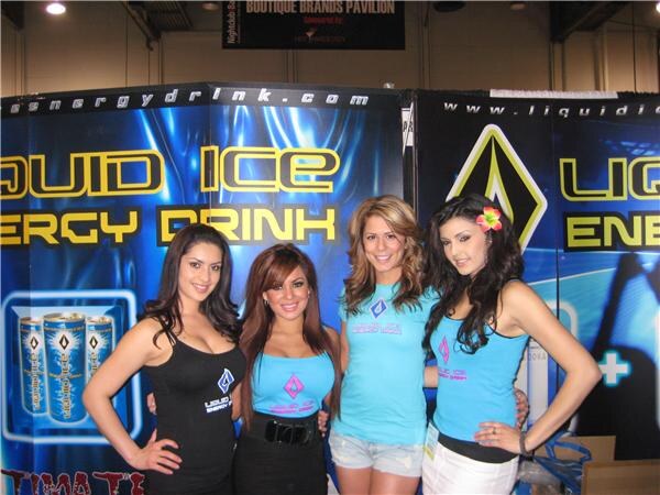 Four women in black and light blue tops stand side by side in front of Liquid Ice Energy Drink banners showing cans. A Boutique Brands Pavilion sign hangs overhead.