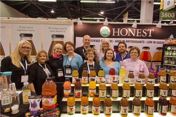 Group of nine people in a row behind a tiered display of Honest Tea bottles, with an Honest USDA Organic banner behind them and a table with bottles in front.