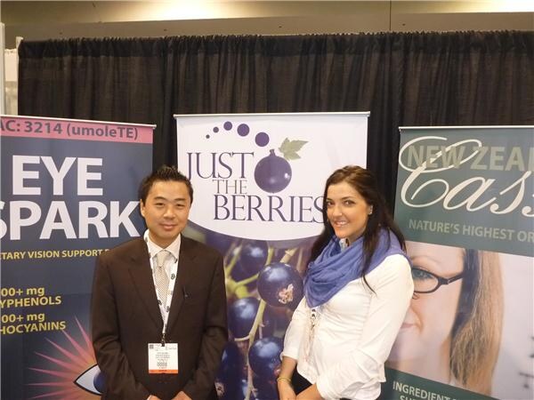 A man in a brown suit and a woman in a white top with a blue scarf stand in front of a Just the Berries banner showing dark berries, with other banners on either side.