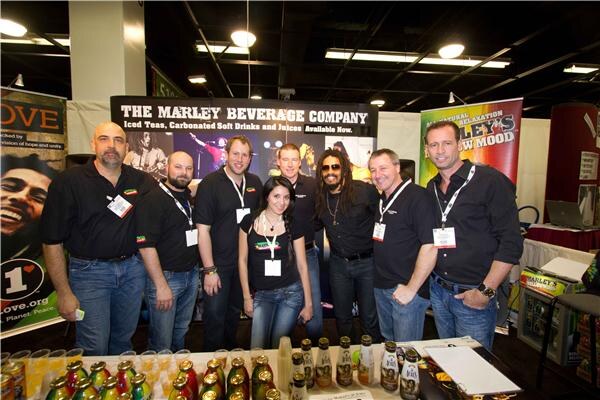 Seven people in black shirts stand behind a table of bottled drinks under a The Marley Beverage Company sign. A Marley's Mellow Mood banner hangs at right.