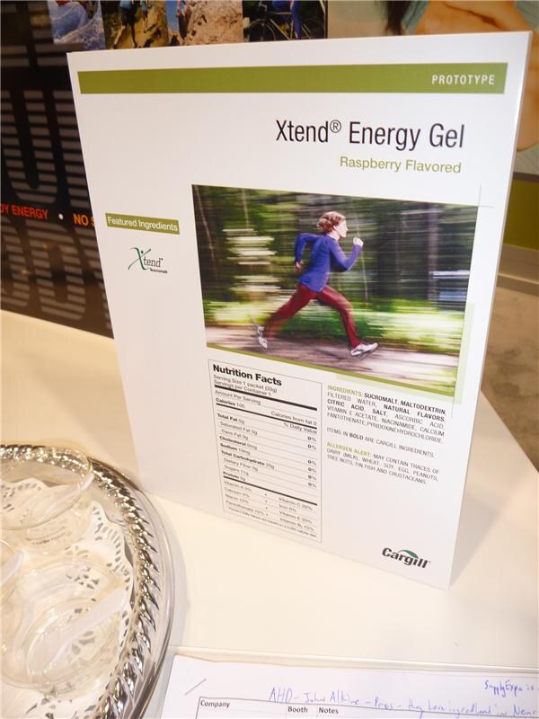 A printed prototype sign for Xtend Energy Gel, raspberry flavored, with a nutrition facts panel, a running woman photo and the Cargill logo, beside a tray.