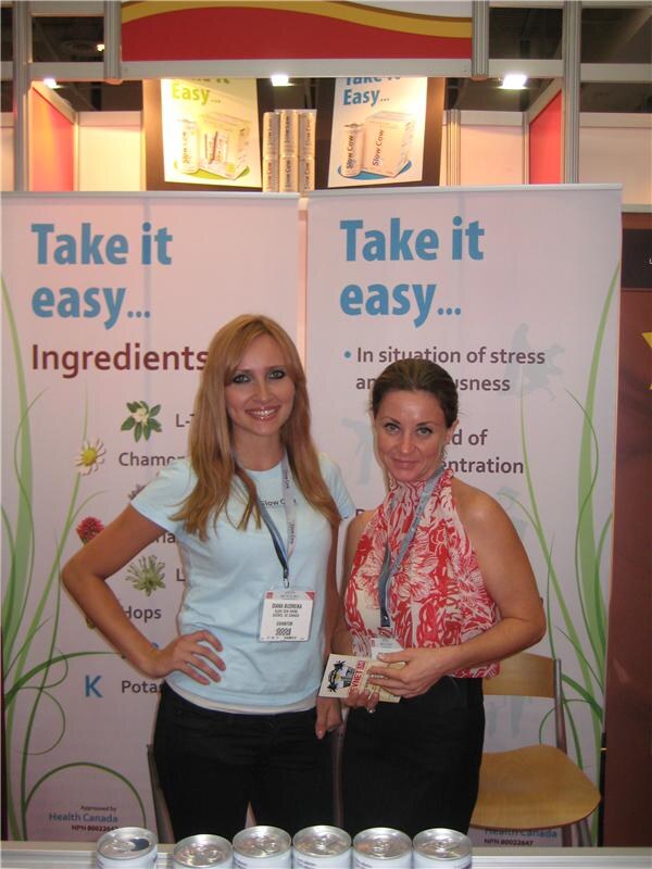 Two women with badges stand in front of Take it easy banners at the Slow Cow booth. Slow Cow cans line the counter in front of them.
