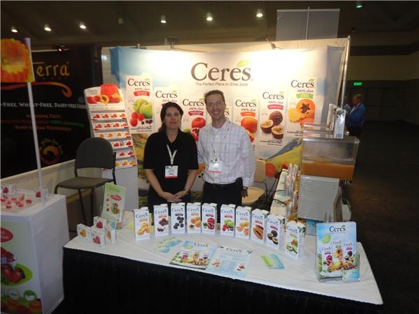A woman in black and a man in a checked shirt stand behind a table of Ceres juice cartons in front of a Ceres backdrop, with a Terra sign at left.