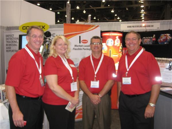 Four people in red polo shirts and lanyards stand together at a booth with Cognex and Bemis signage behind them. Two men flank a woman and another man.