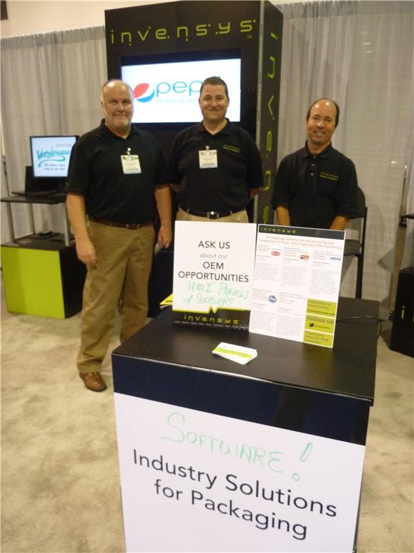 Three men in black polo shirts stand behind a counter at the Invensys booth, with a Pepsi logo on a screen behind them and a sign reading Industry Solutions for Packaging.
