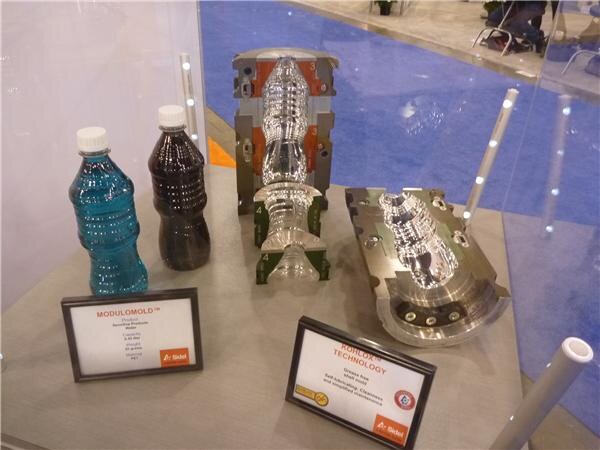 Display case with two filled bottles, metal blow mold sections and Sidel signs for Modulomold and another technology.