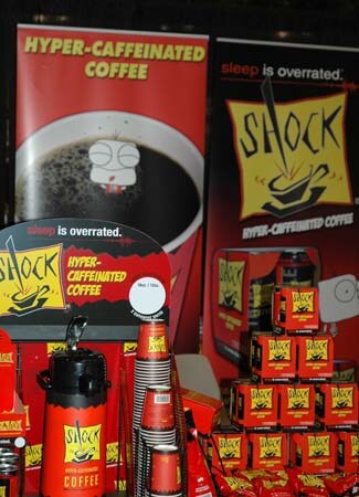 Shock Coffee display with red banners reading Hyper-Caffeinated Coffee, stacked red boxes, paper cups and a red airpot dispenser.