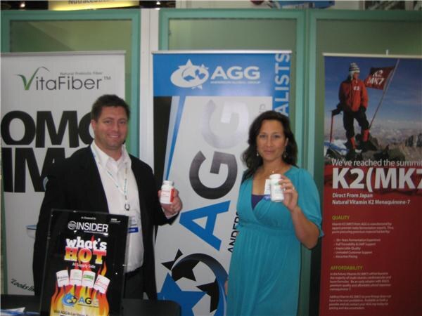 A man and a woman hold supplement bottles in front of AGG, VitaFiber and K2(MK7) banners, with an Insider What's Hot sign in the foreground.