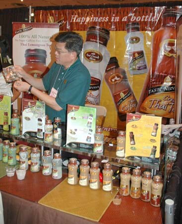 A man in glasses and a green shirt examines a small package at a Taste Nirvana booth with bottled coffee and tea drinks on glass shelves.