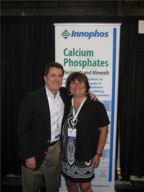 A man in a dark blazer and a woman in a patterned dress, both with badges, pose together in front of an Innophos banner about calcium phosphates.