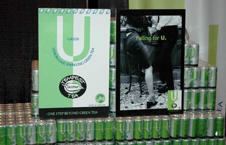 Tempest Tea lemon-lime sparkling green tea sign and a Falling for U poster in front of stacked green cans.