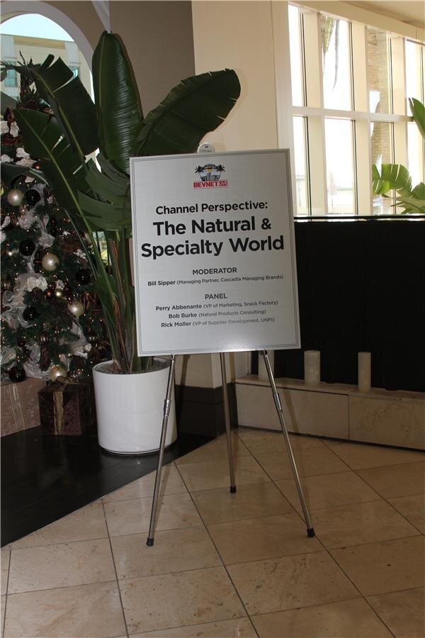 A sign on an easel reads Channel Perspective: The Natural & Specialty World, listing a moderator from Cascadia Managing Brands and panelists from Snack Factory, Natural Products Consulting and UNFI.