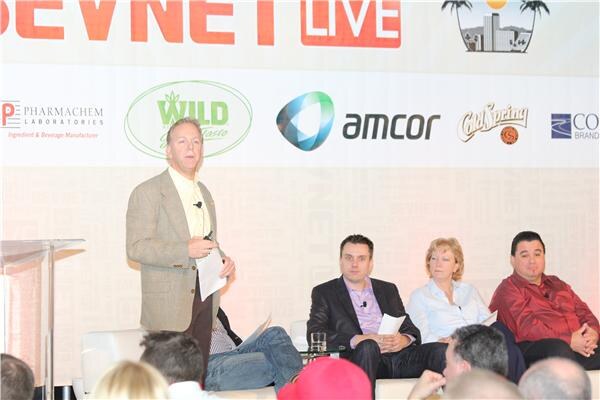 Kevin Wright of Raley's stands at left holding papers and speaking, while a man, a woman and another man sit nearby on white seating in front of a BevNET LIVE sponsor backdrop.