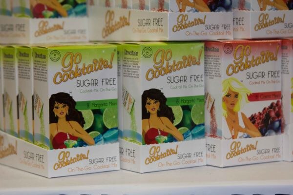 Stacked boxes of Go Cocktails! sugar free on-the-go cocktail mix, with illustrated women on the packaging. Margarita mix boxes sit at left and center, and a red-labeled flavor is at right.