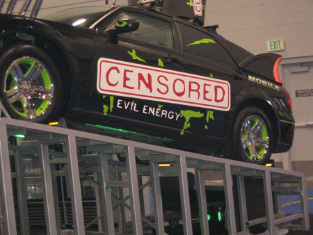 A black car with a Censored Evil Energy logo and green splatter graphics sits on an elevated metal truss platform. A Mobil logo appears near the rear window.