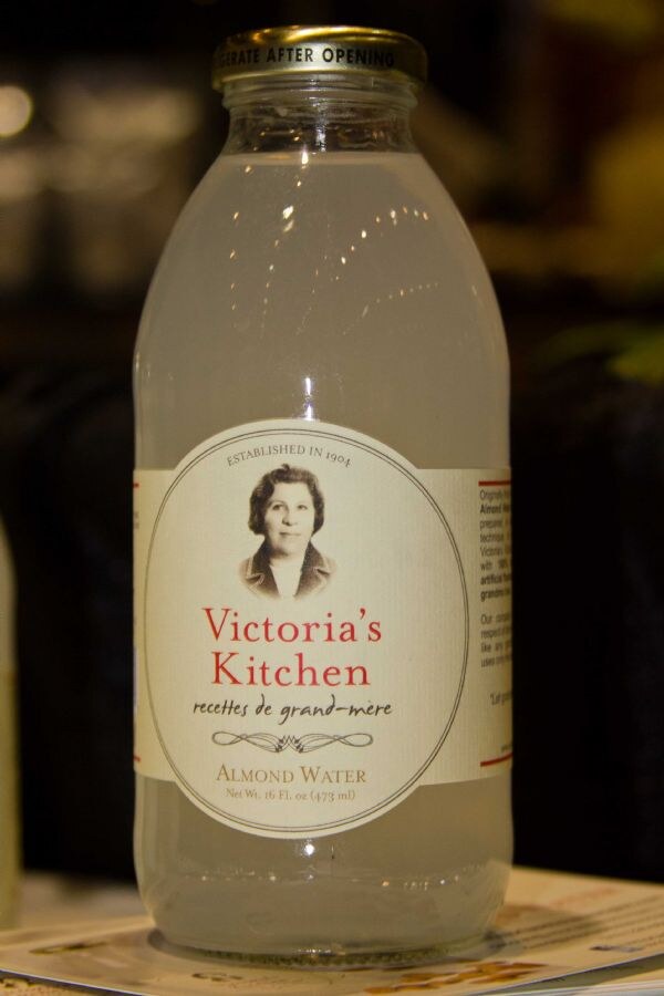 Close view of a glass bottle of Victoria's Kitchen Almond Water, 16 fl oz, with a label showing a vintage portrait and the text Established in 1904.